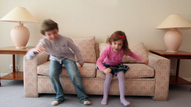 Two kids come in room, sit and jump on sofa