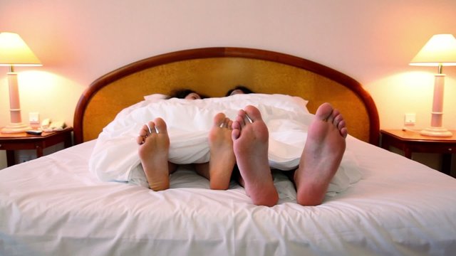 Couple lays in bed under blanket