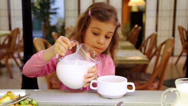 Little girl takes jug with milk and pours it in plate