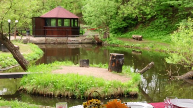 Dining table is set in bower ashore of small pond