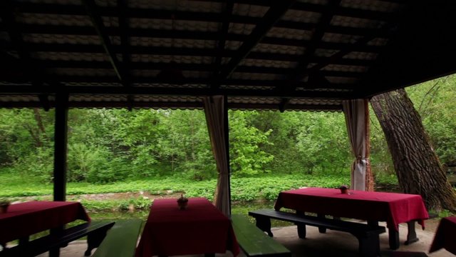Five tables in bower ashore of small pond at among trees