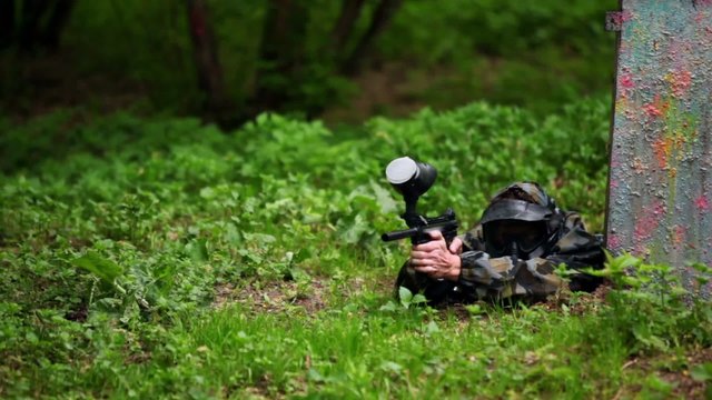 Boy paintball player lies with gun in ambush on grass
