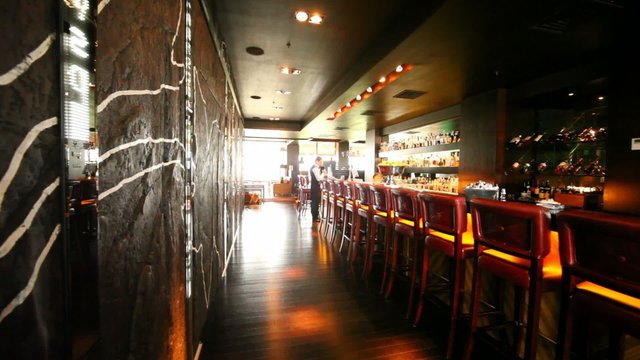 Many chairs stands along bar counter where man sits