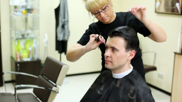 Hairdresser cuts hair to man with long hair by scissors