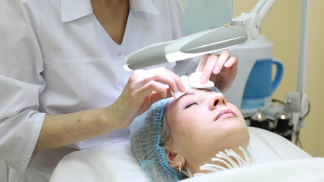 Beautician does disinfection of forehead by cotton pads