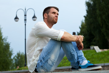 Fototapeta premium Young tired man sit on border in summer park