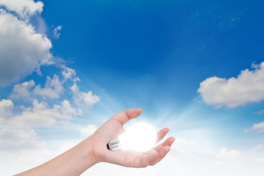 Women hand with lamp bulb against the blue sky.