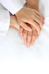 Woman holding senior woman's hand on bed