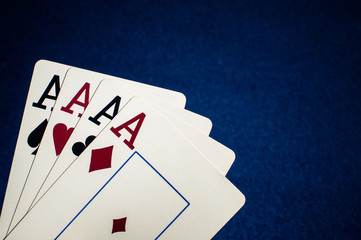Four ace playing cards arranged on blue fabric background