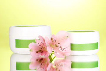 Jars of cream with flower on green background