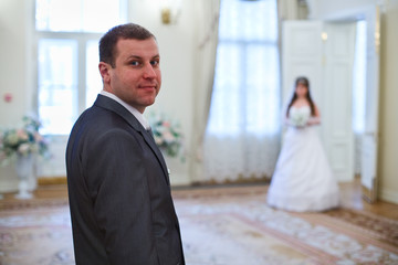 Groom  on foreground, bride in room on background