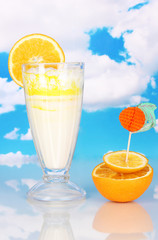 Delicious milk shake with orange on table on sky background