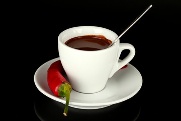 white cup with hot chocolate and chili pepper isolated on black