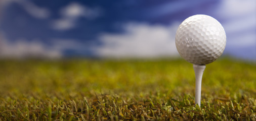 Golf ball on green grass over a blue sky 