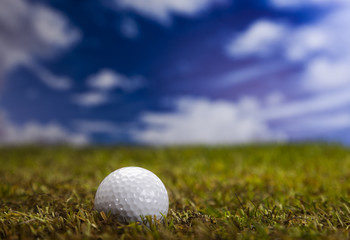 Golf ball on green grass over a blue sky 