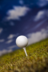 Golf ball on green grass over a blue sky 