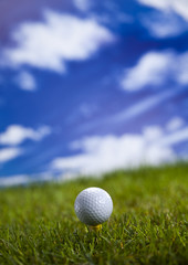 Golf ball on green grass over a blue sky 
