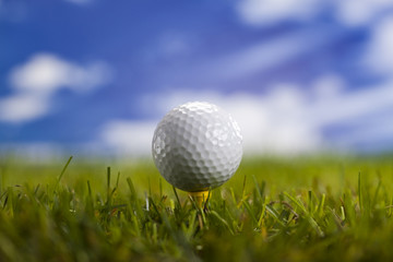 Golf ball on green grass over a blue sky 