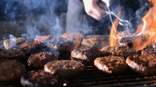 hamburgers cooking on a barbeque grill with flames and smoke
