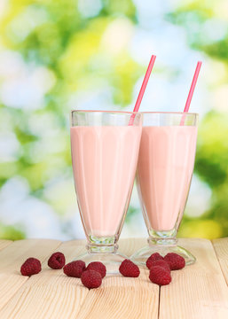 Raspberry milk shakes on wooden table on bright background