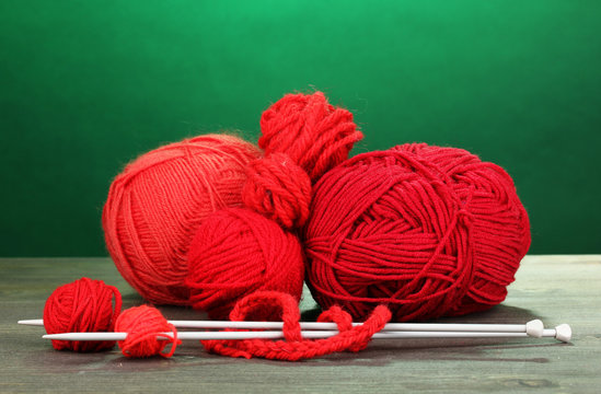 Red knittings yarns on wooden table on green background