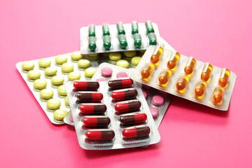 Capsules and pills packed in blisters, on pink background