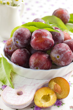 Fresh wet plums with leaves in the bowl on the vintage board