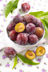 Fresh wet plums with leaves in the bowl on the vintage board
