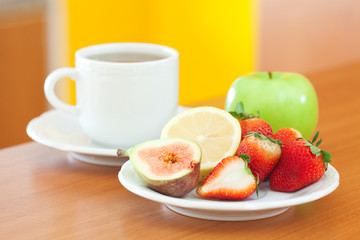 cup of tea,cookie,apple, lemon, fig and strawberries on a plate