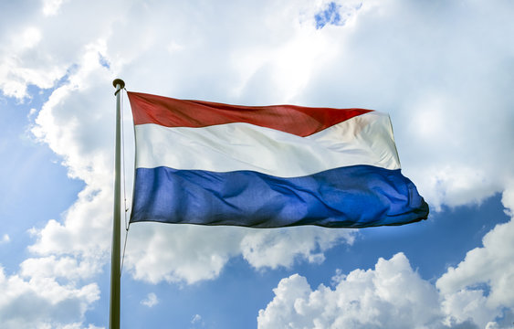Waving flag of The Netherlands on the flagpole against cloudy bl