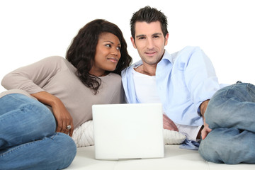 Couple lying on a bed  looking at a laptop