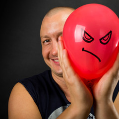 Happy man hiding behind angry balloon