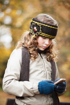 Girl texting with cellphone in an autumn park
