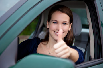 Attraktive junge Frau im Auto zeigt Daumen hoch