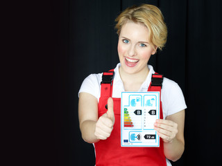 Female car mechanic showcases tire label and has thumb up