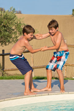 Kinder spielen am Swimmingpool - Jungen stoßen sich in den Pool
