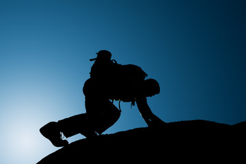 Silhouette of climbing young adult at the top of summit