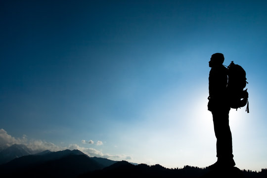 Silhouette of climbing young adult at the top of summit