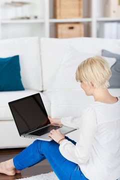 blonde frau sitzt mit laptop auf dem sofa
