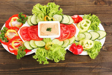 Chopped vegetables and sauce on plate on wooden table