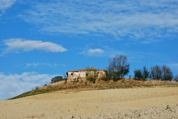 rudere nella campagna toscana con cielo azzurro e nubi