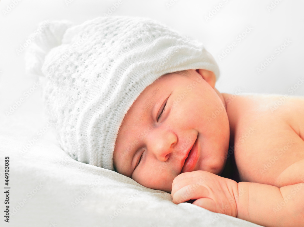 Wall mural smiling newborn baby in white hat