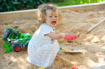 girl is playing in a sandbox - obrazy, fototapety, plakaty