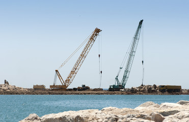 Fototapeta premium Building a dike. Cranes and excavator put stones