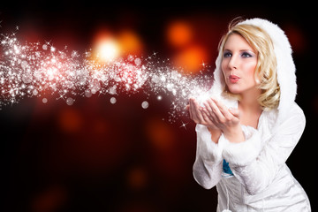 junge blonde Frau im Winteroutfit pustet Schnee