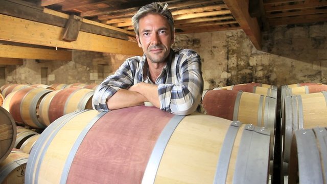 Smiling winemaker leaning on wine barrel in winery