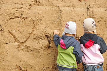 two children draw on the sand wall