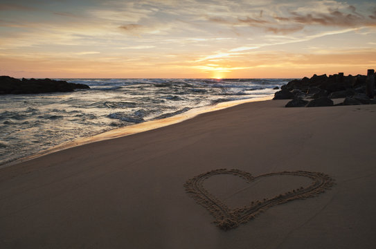 heart drawn in the sand on the beach at sunset