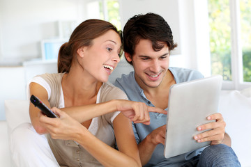 Cheerful couple choosing tv program on digital tablet