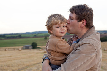 Fototapeta premium Young father giving son kiss on golden straw field
